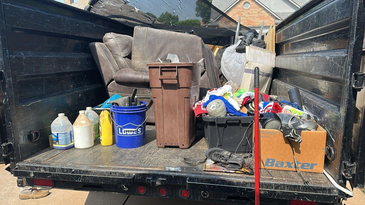 A truck bed loaded with a recliner, a trash can, buckets, bins and boxes of household junk