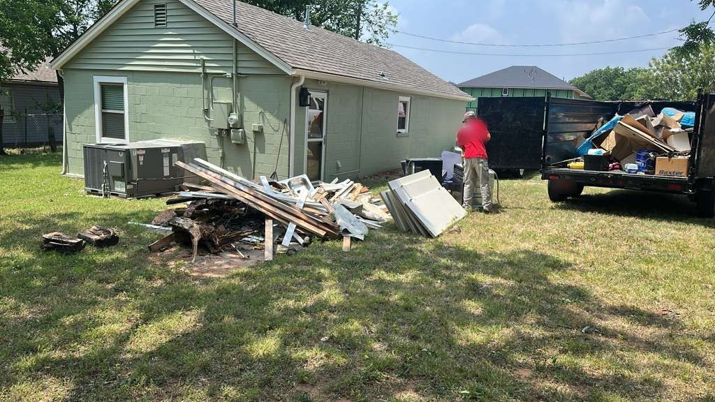 Before: a pile of old lumber, boards and siding on the lawn behind a green house