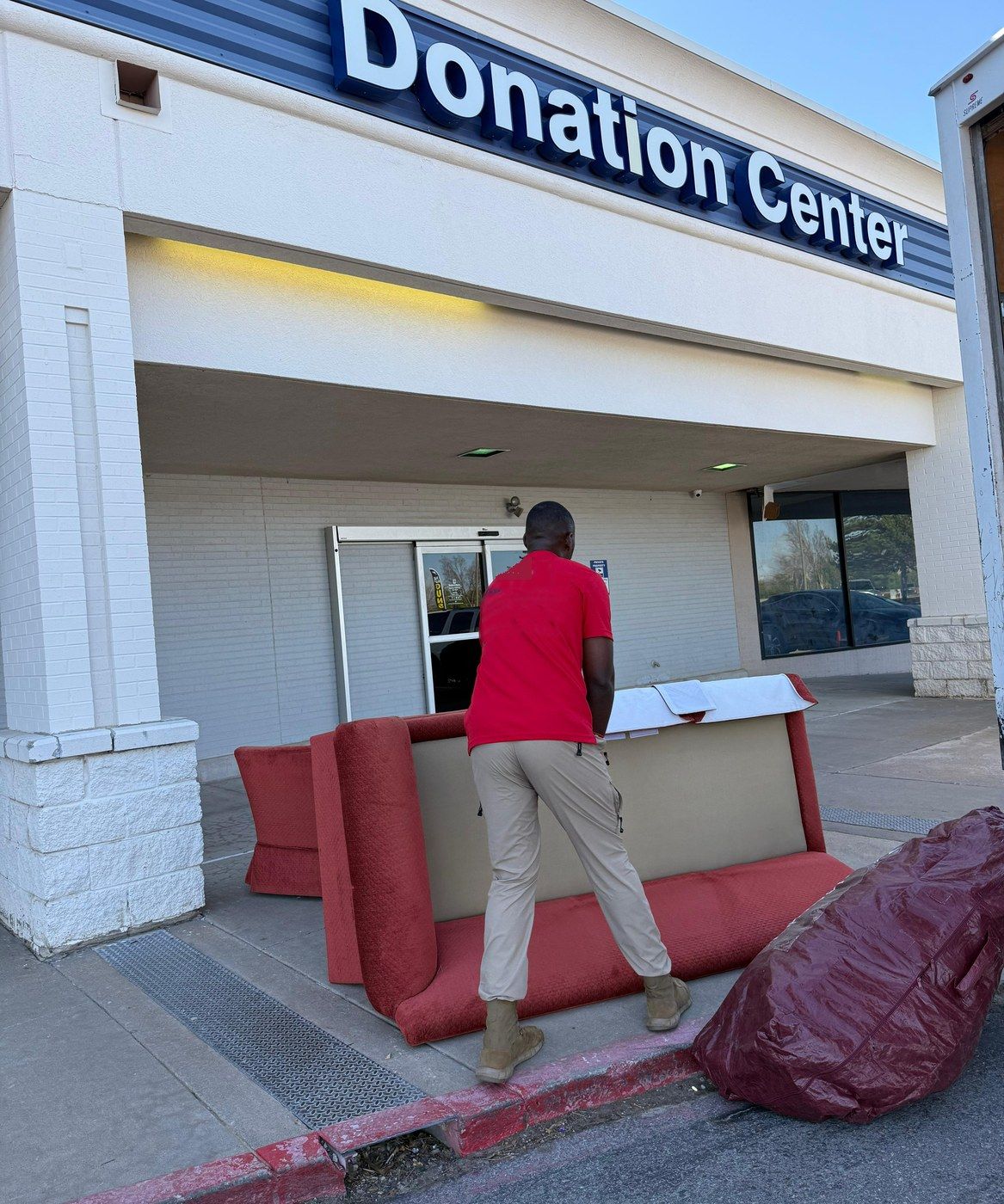 A crew member unloading a red sofa at a donation center drop-off