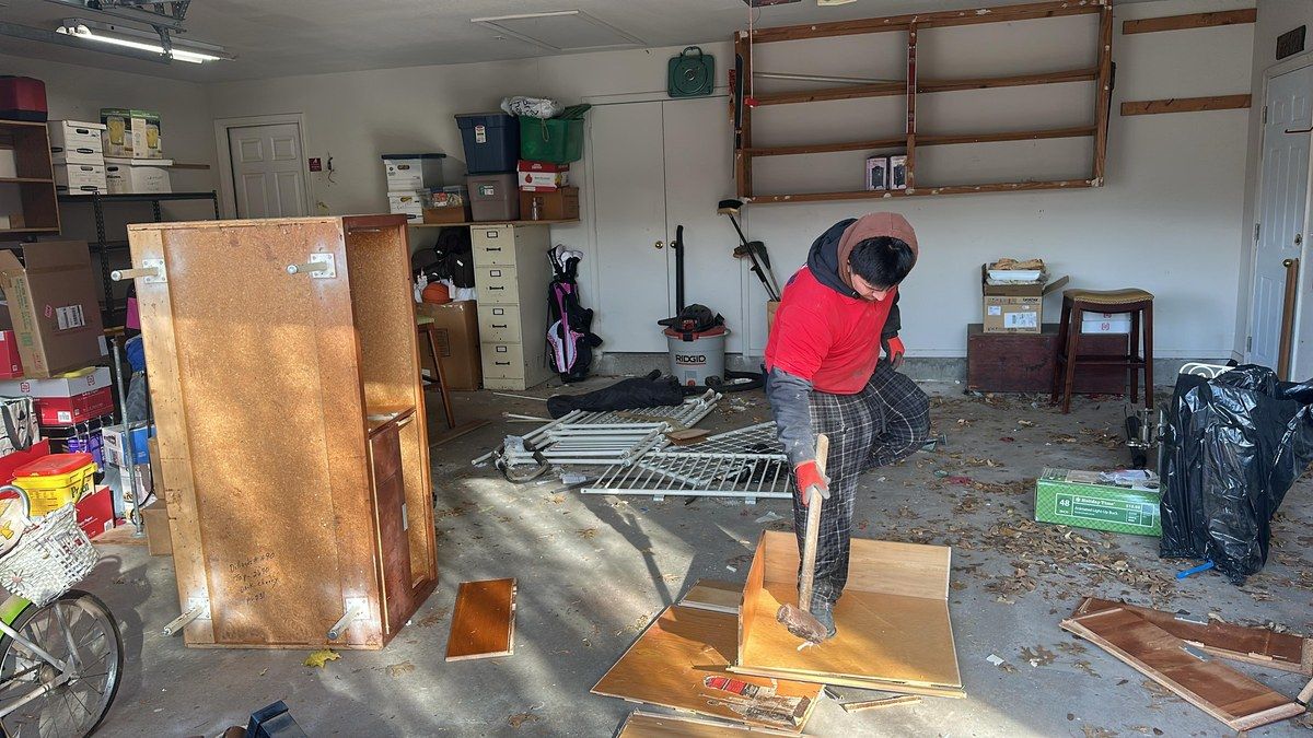A crew member breaking down an old wooden cabinet during a garage cleanout