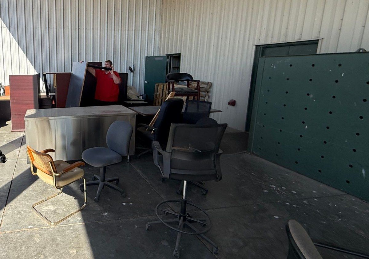 Office desks and rolling chairs gathered on a loading dock for removal