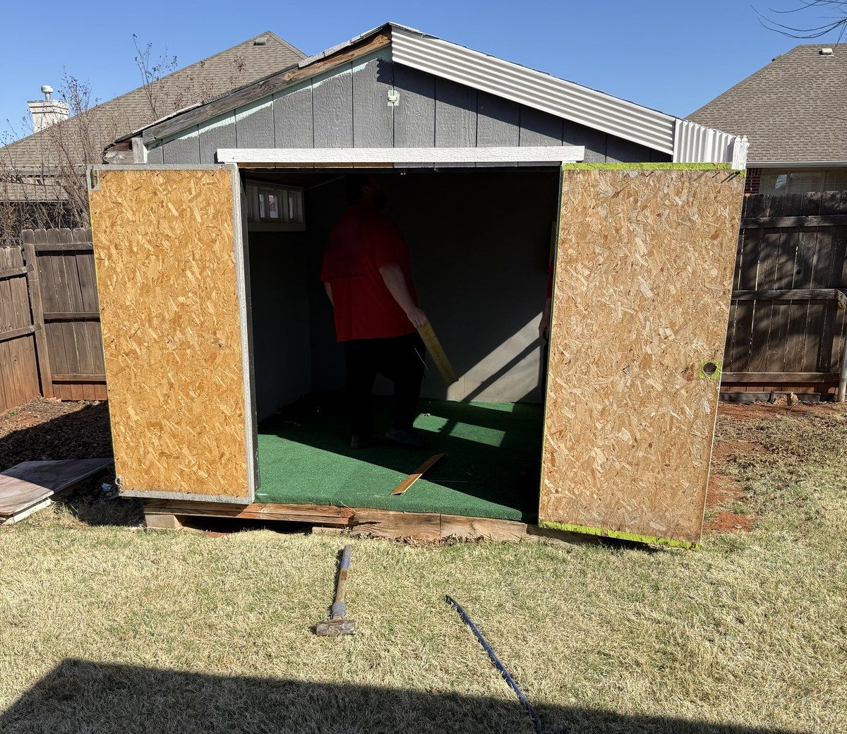 A crew member inside a backyard shed with its wooden doors removed for demolition