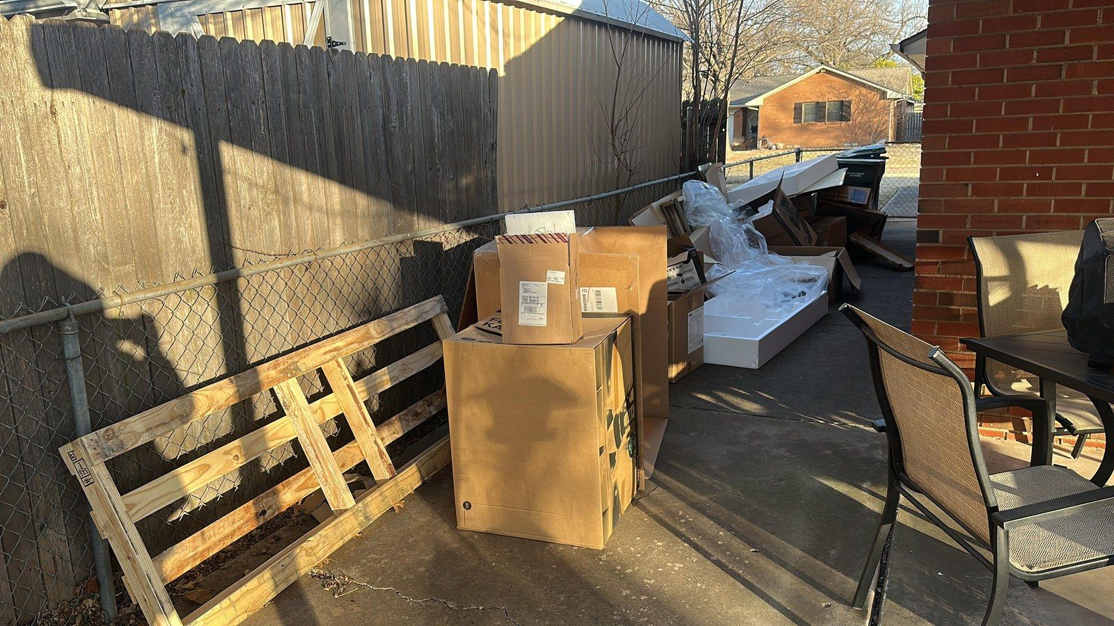 Before: pallets, cardboard boxes and furniture piled along a fence beside a brick house