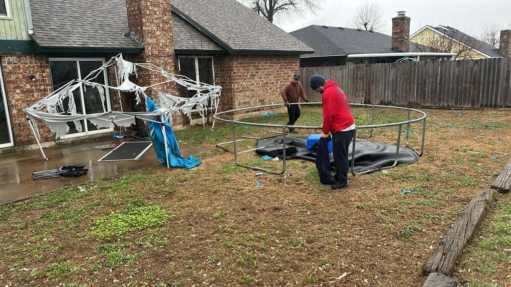 Two crew members taking apart a storm-damaged trampoline in a backyard